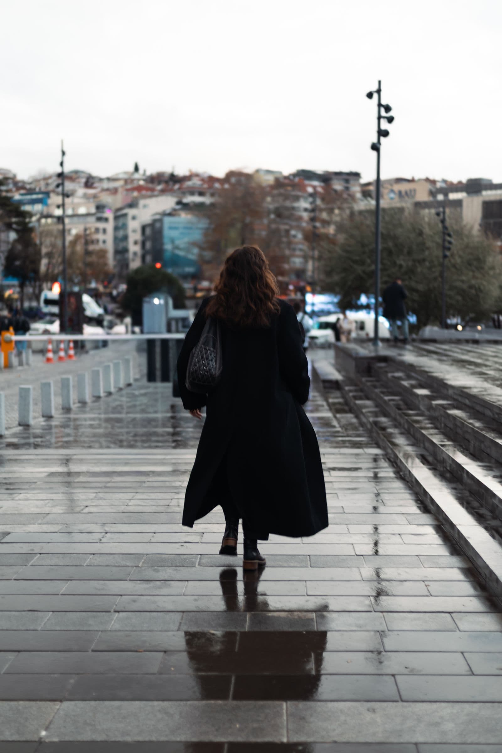 Woman in a dark coat walking on a wet city street