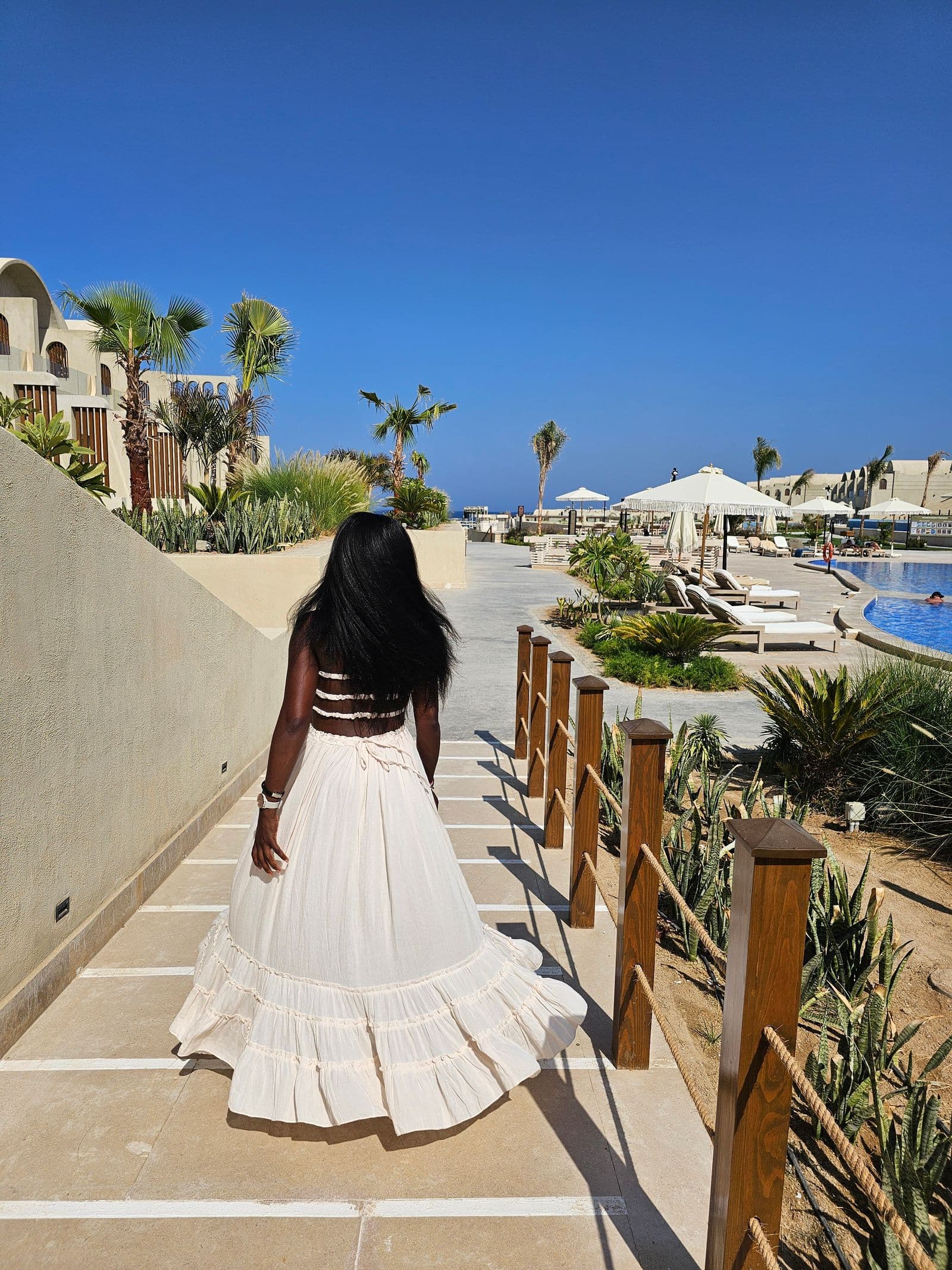 Woman walking beside a resort pool in an elegant summer outfit